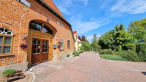 A brick building with a large wooden door, a small window with a flower basket, and a sign with the number 1858. - Vacation apartment Ackerblick on a beautiful vacation farm near the Baltic Sea (Schwartbuck)