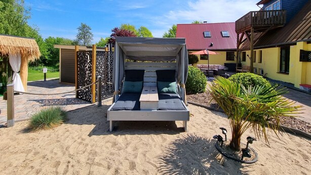 A bed with a canopy in a sandy outdoor area, surrounded by a wooden fence and a thatched structure. - Vacation apartment Ackerblick on a beautiful vacation farm near the Baltic Sea (Schwartbuck)