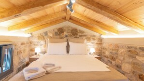 A cozy bedroom with a stone wall, wooden ceiling beams, a large bed, and two bedside lamps.
