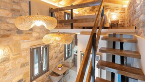A rustic interior with exposed wooden beams, stone walls, and a wooden staircase.