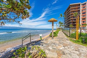 Un hotel frente a la playa con un camino de piedra, una sombrilla de paja y vista al océano.