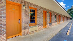 A row of brick buildings with orange doors and windows, a covered walkway, and a parking area. - Hotel O Deluxe Inn Kingstree Sc Hwy 52 (Kingstree)