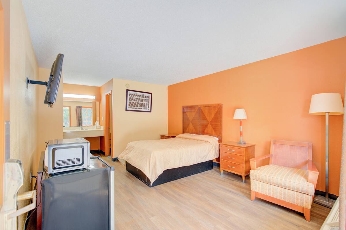 Une chambre d’hôtel équipée d’un lit, d’une chaise, d’un bureau avec un ordinateur, d’une télévision et d’une lampe.