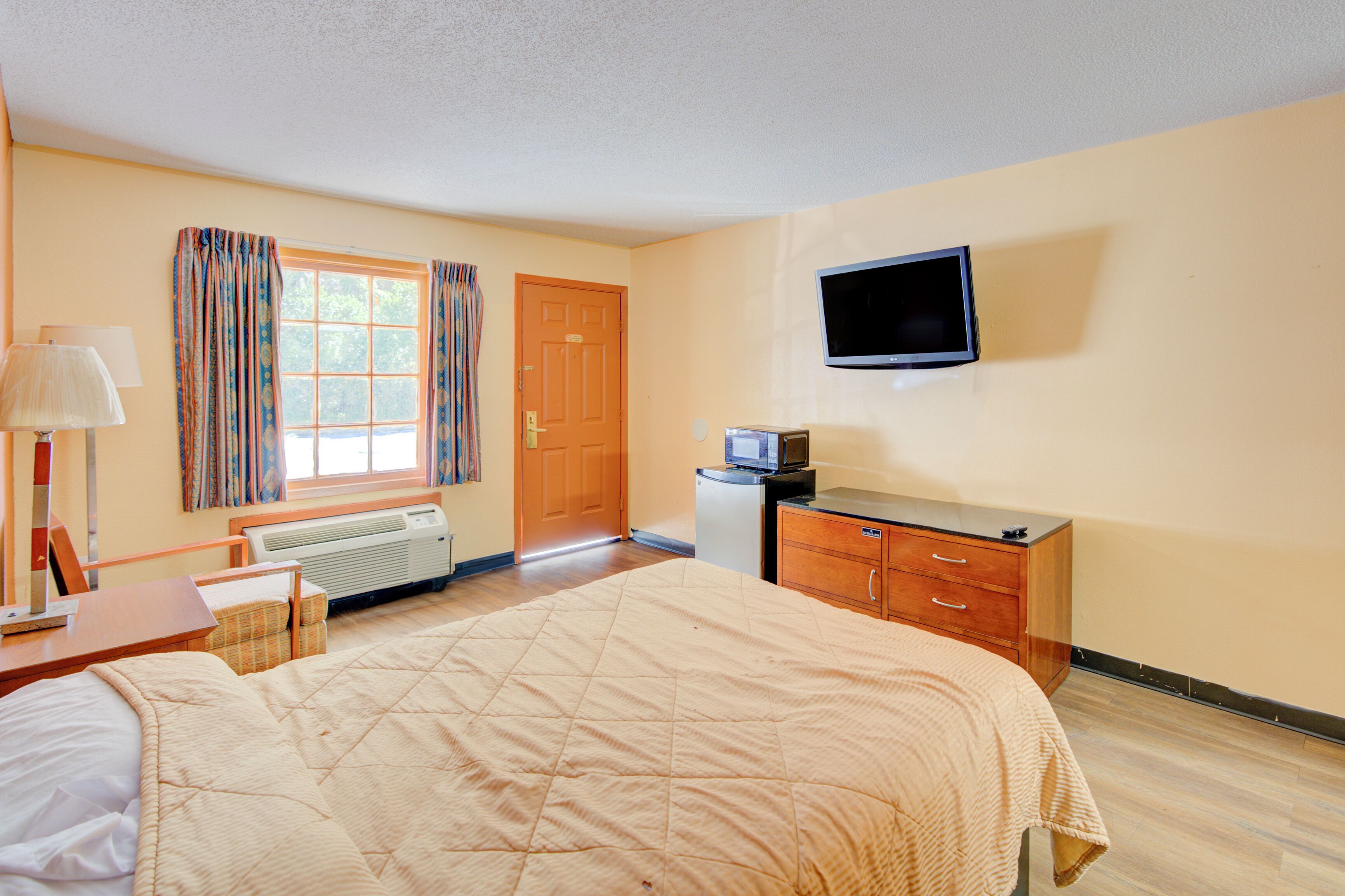 Une chambre d’hôtel équipée d’un lit, d’un bureau, d’une télévision et d’une fenêtre avec des rideaux.