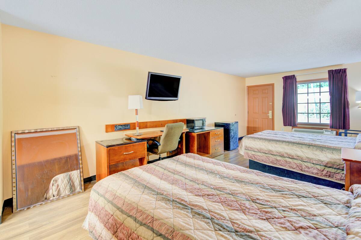 Une chambre d’hôtel avec deux lits, un bureau avec un ordinateur, une télévision et une fenêtre avec des rideaux.