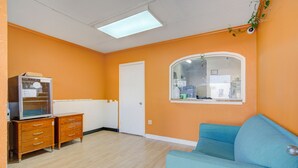 A room with orange walls, a blue sofa, a wooden cabinet, and a window with a view. - Hotel O Deluxe Inn Kingstree Sc Hwy 52 (Kingstree)