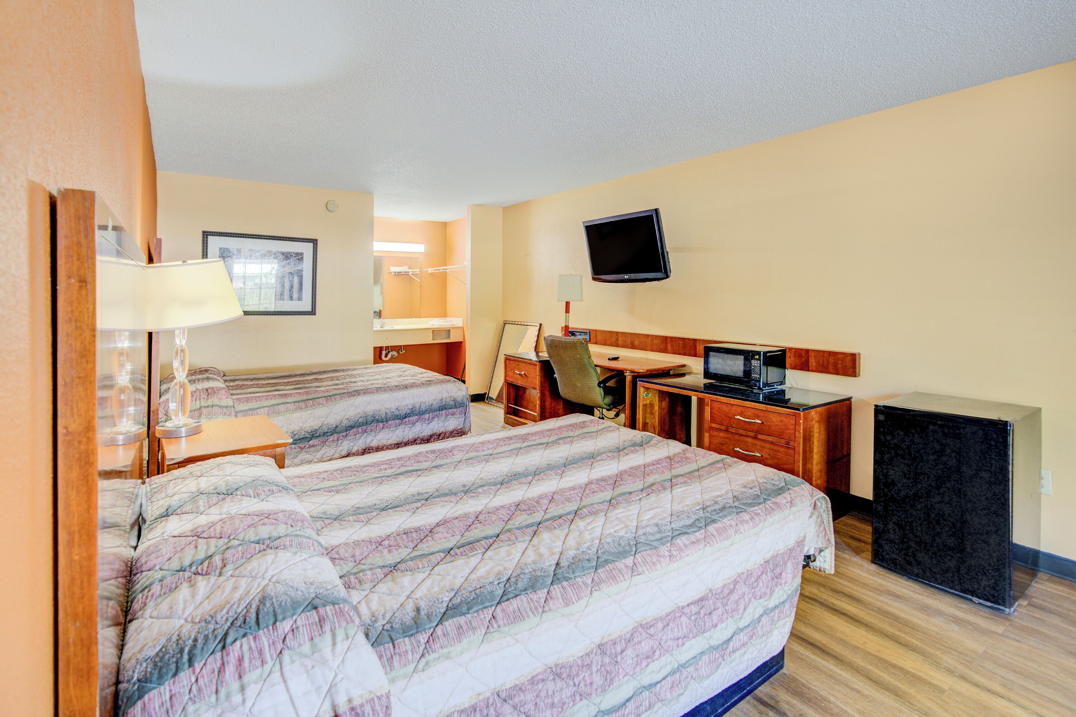 A hotel room with two beds, a desk, a chair, a TV, a dresser, and a small refrigerator.