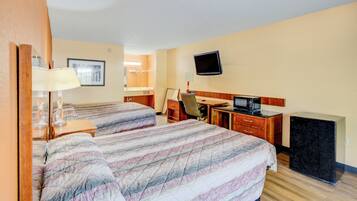 A hotel room with two beds, a desk, a chair, a TV, a dresser, and a small refrigerator.