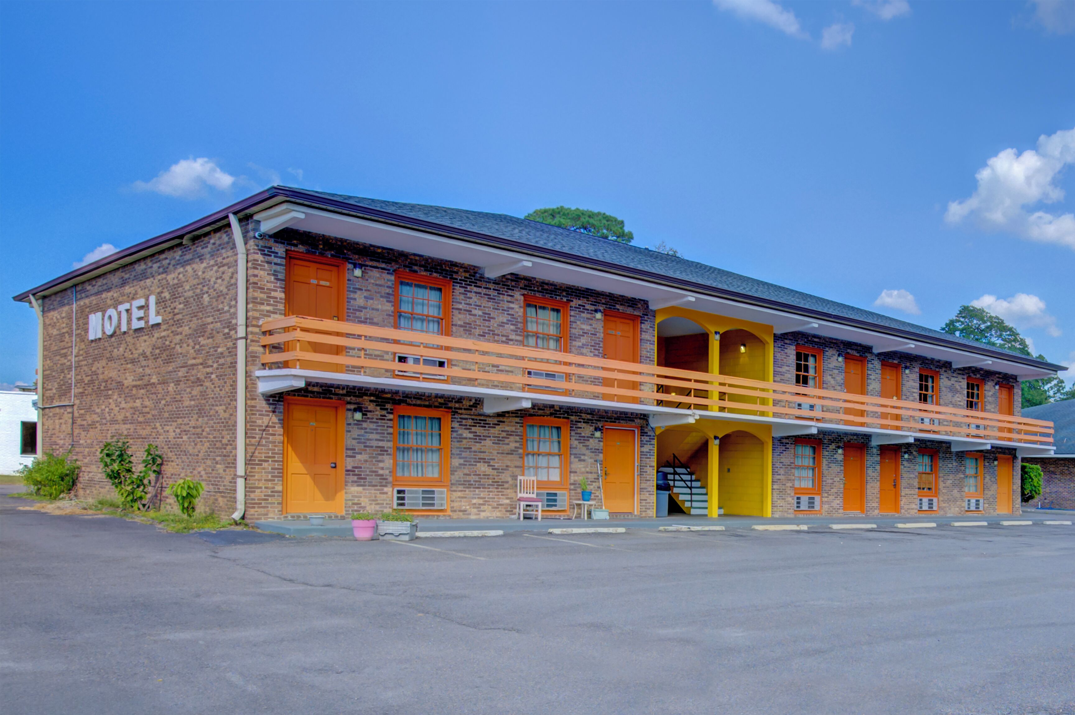 Un motel con fachada de ladrillo, puertas anaranjadas y un corredor cubierto.