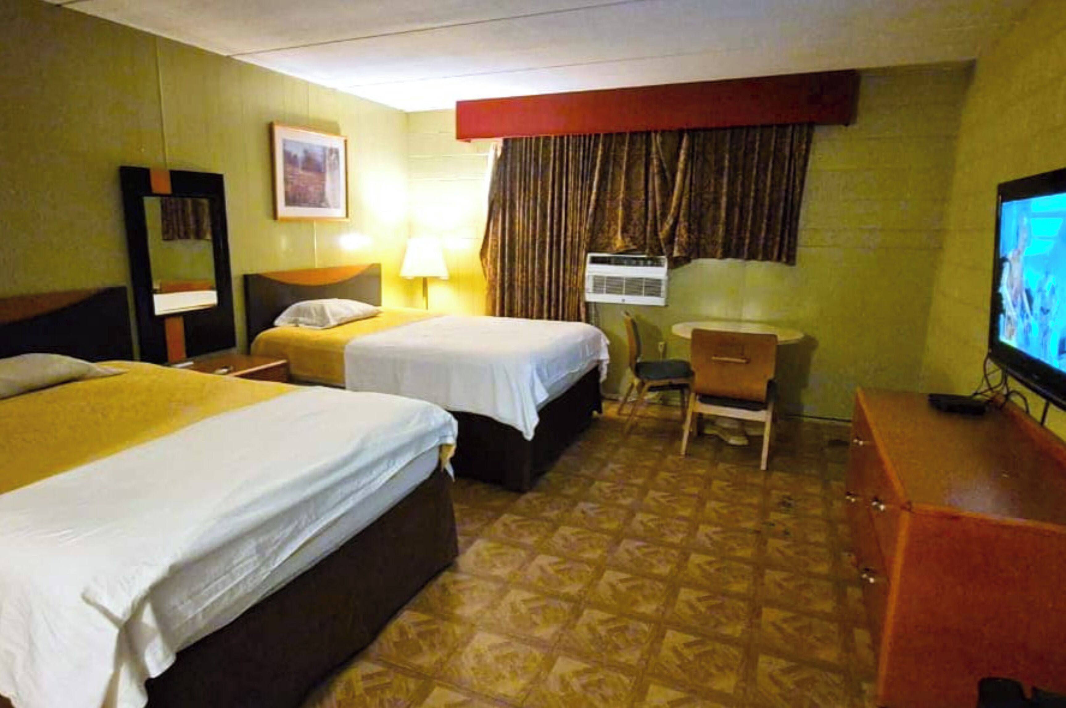 Une chambre d’hôtel avec deux lits, un bureau, une chaise, une télévision et une fenêtre avec des rideaux.