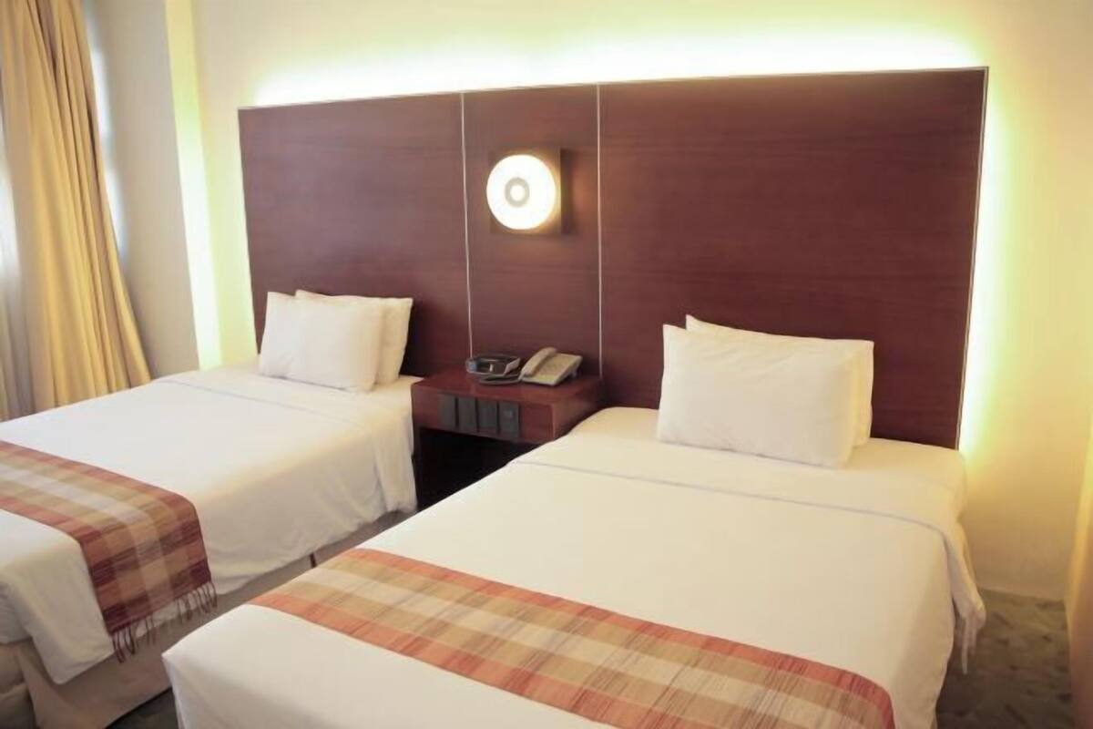 Habitación de hotel con dos camas, una mesita de noche con teléfono y una lámpara fijada a la pared.