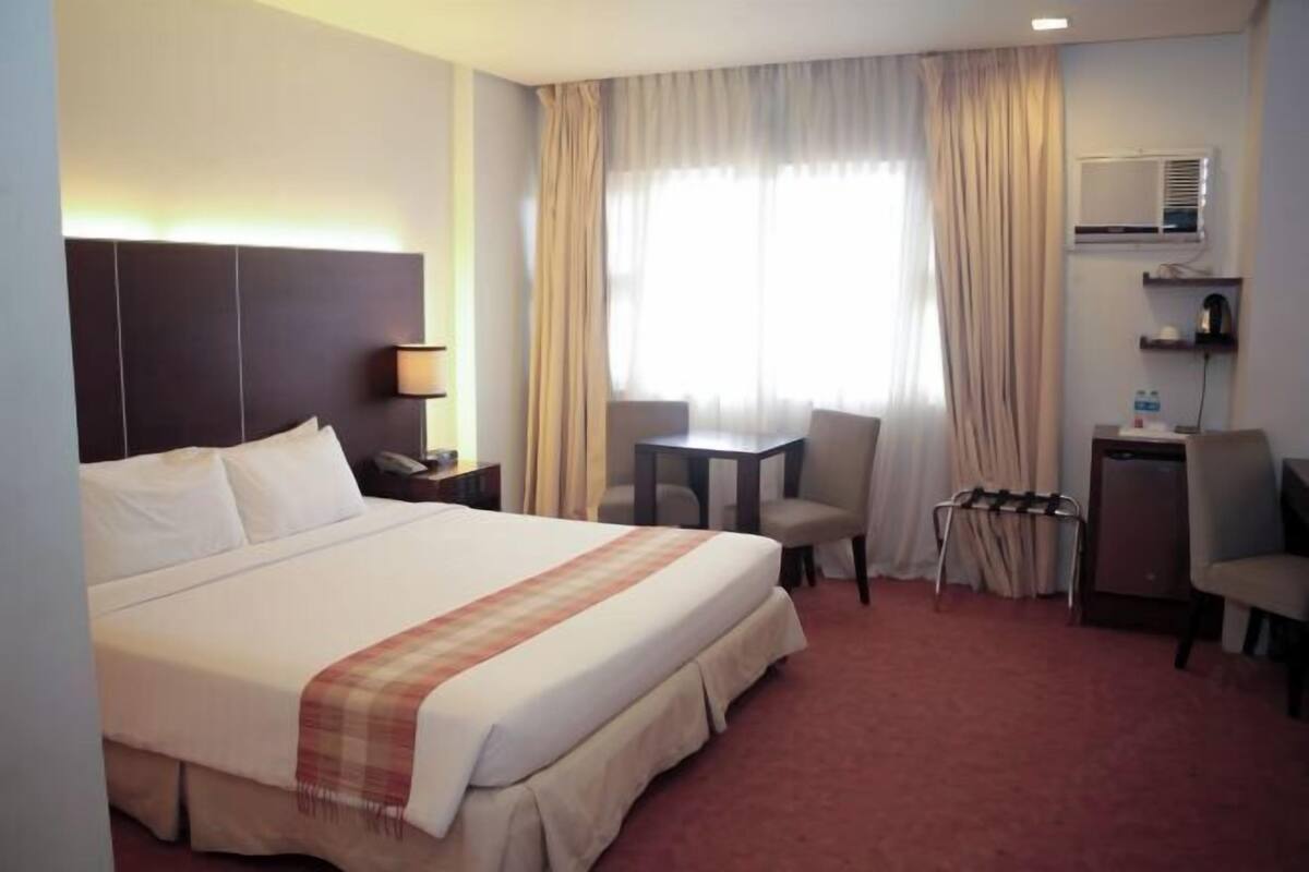 Una habitación de hotel con una cama grande, un escritorio, una silla, una mesita y un espejo en la pared.