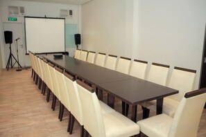 A conference room with a long table and chairs, a projector screen, speakers, and an exit sign. - Casablanca Suites Near Airport (Legaspi)