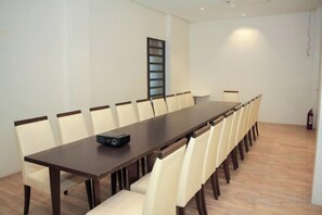 A conference room with a long table, chairs, a projector, and a fire extinguisher.