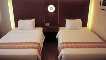 A hotel room with two single beds, a nightstand with a phone, and a wall-mounted light fixture.