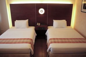 Une chambre d’hôtel avec deux lits simples, une table de chevet avec un téléphone et un luminaire fixé au mur.