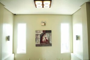 A bathroom with a light-colored wall, a ceiling light fixture, a framed artwork, and a window.