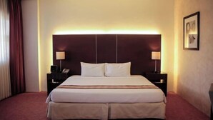Ein Hotelzimmer mit einem großen Bett, Nachttischen, einem Kopfteil und einem gerahmten Bild an der Wand.