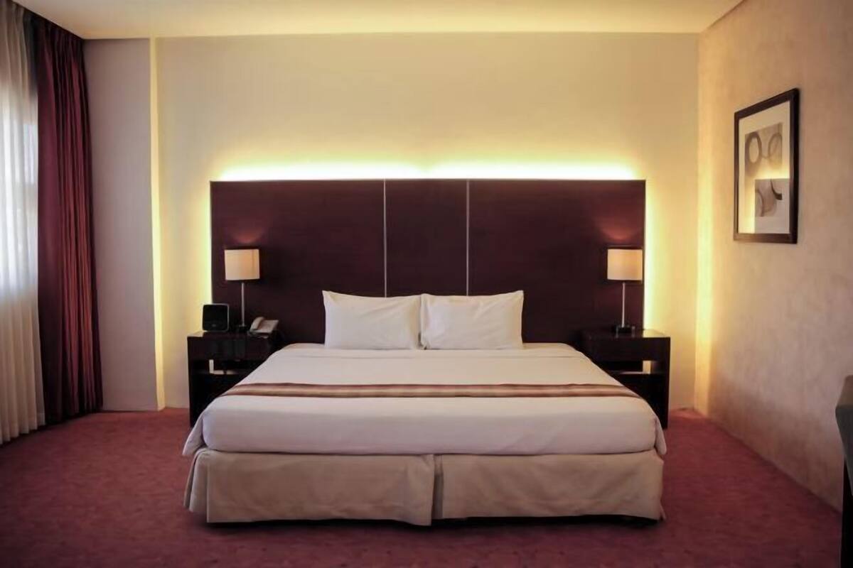 Habitación de hotel con una cama grande, mesitas de noche, cabecera y un cuadro enmarcado en la pared.
