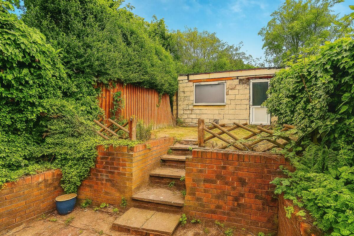 A small brick house with a wooden staircase leading to a door, surrounded by dense greenery.