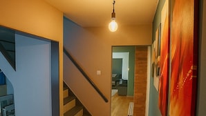 Et moderne interiør med en trappe, der fører op til en anden etage, en gang med kunst og et synligt køkkenområde.