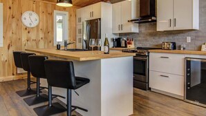 Une cuisine moderne dotée d’un îlot central, de meubles blancs, d’appareils électroménagers en acier inoxydable et de tabourets de bar noirs.