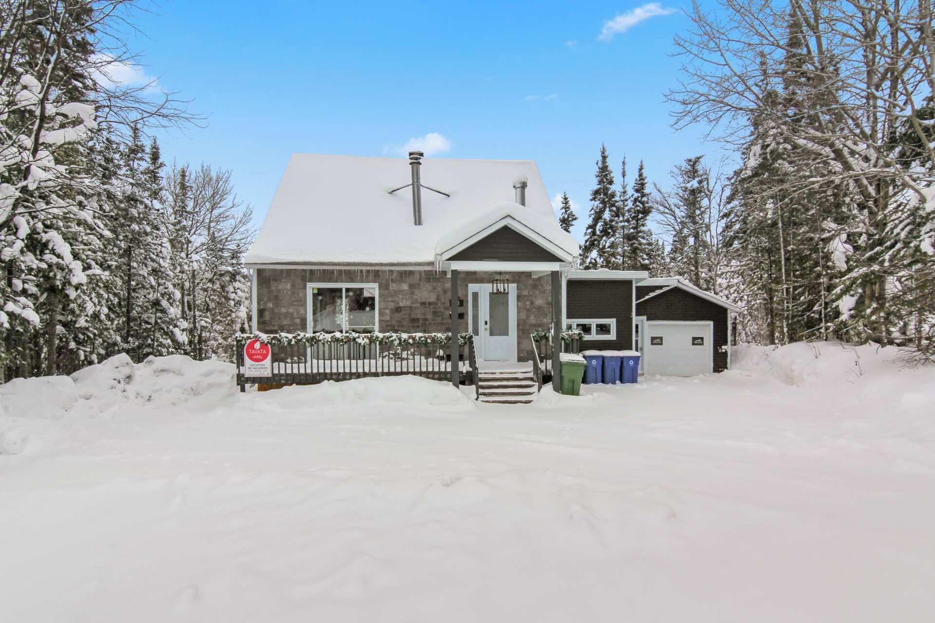 Une maison à deux étages, dont le toit est recouvert de neige, avec un porche à l’avant et un garage.