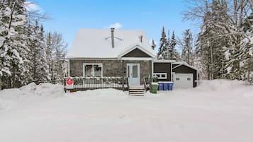 Une maison à deux étages, dont le toit est recouvert de neige, avec un porche à l’avant et un garage.