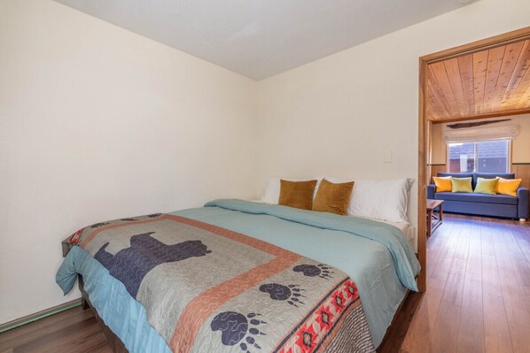 Een slaapkamer met een bed, een houten vloer, een raam en een bank in de aangrenzende kamer.