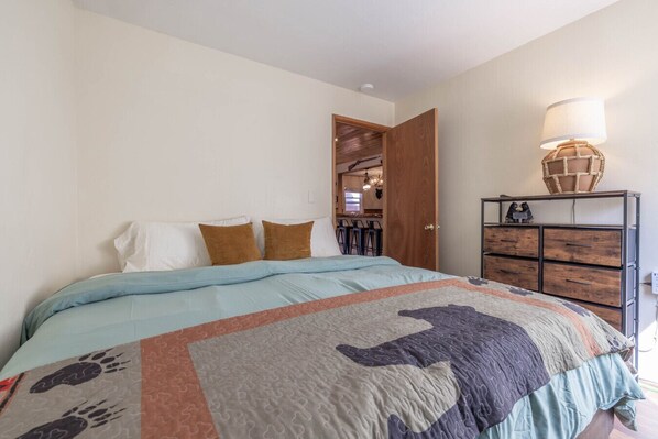 A bedroom with a bed, a wooden dresser, and a lamp.