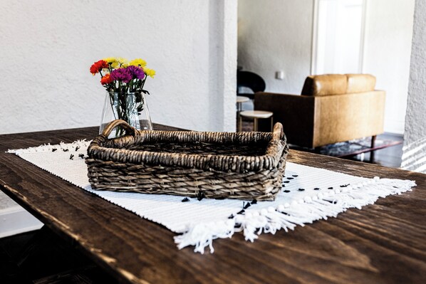 Un panier en osier rempli de fleurs, posé sur une table en bois recouverte d’une nappe en dentelle blanche.