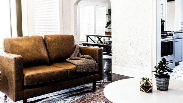A living room with a brown leather sofa, a patterned rug, and a small round table. - Quaint 3BR - Minutes to Downtown San Angelo - Sleeps 6 (San Angelo)