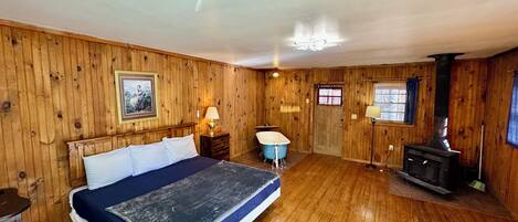Una habitación con paredes de madera, una cama, una bañera y un estufa de leña.