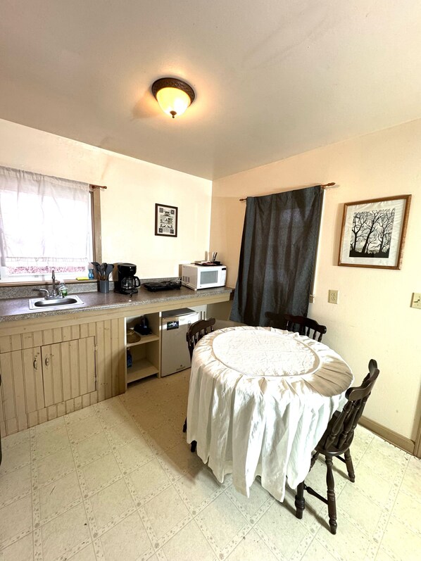 A compact kitchen with a dining area, a microwave, a coffee maker, and a small refrigerator. - Parkview Lodge & Cabins (Newland)
