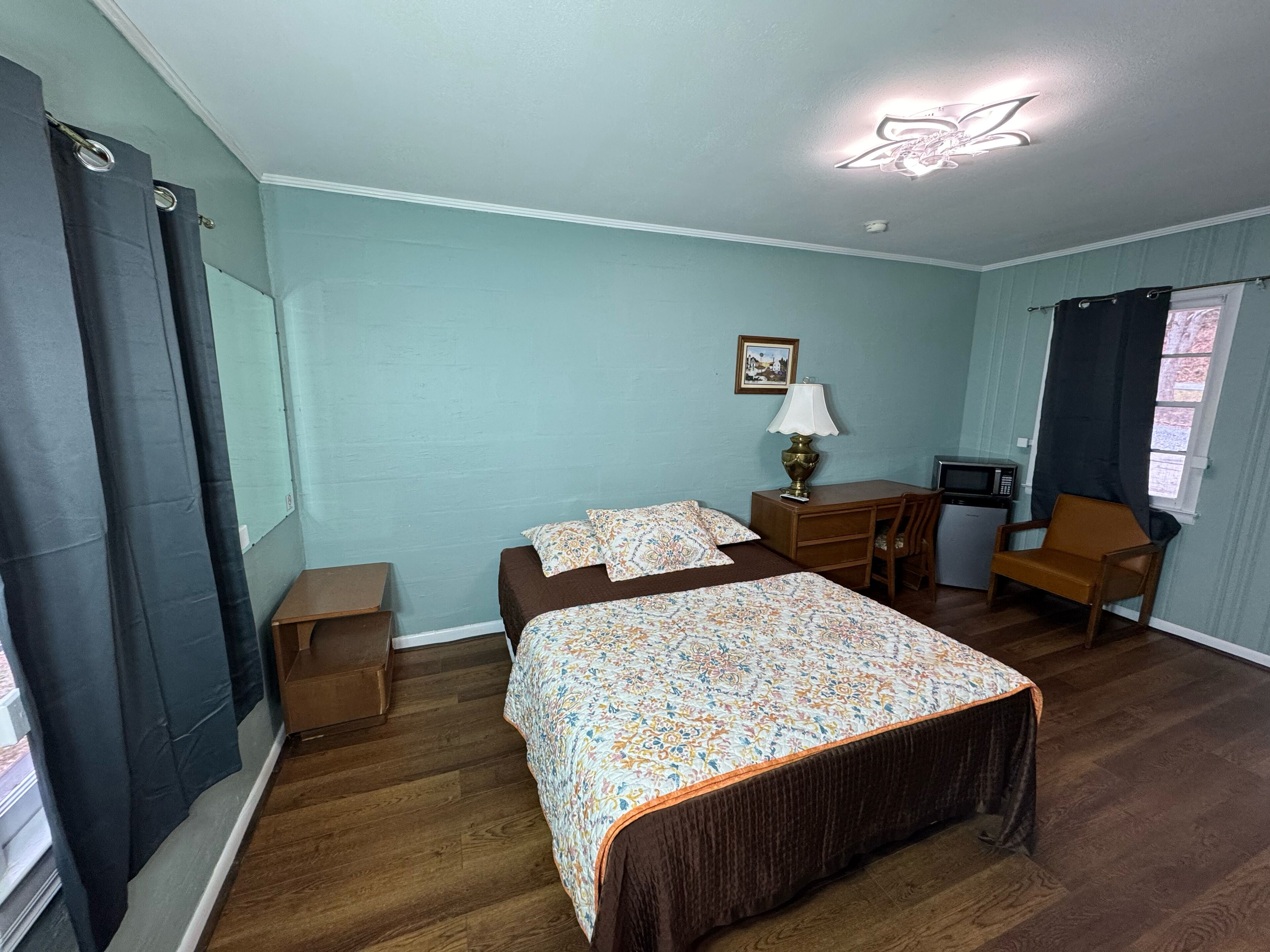 A bedroom with a bed, a desk, a chair, a lamp, and a small table.