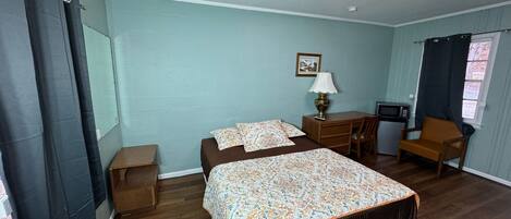 A bedroom with a bed, a desk, a chair, a lamp, and a small table.