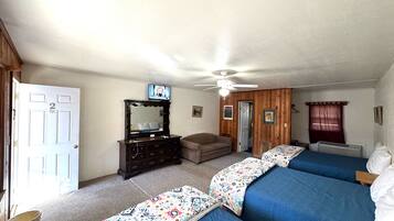 A bedroom with two beds, a dresser, a ceiling fan, and a television on the wall.