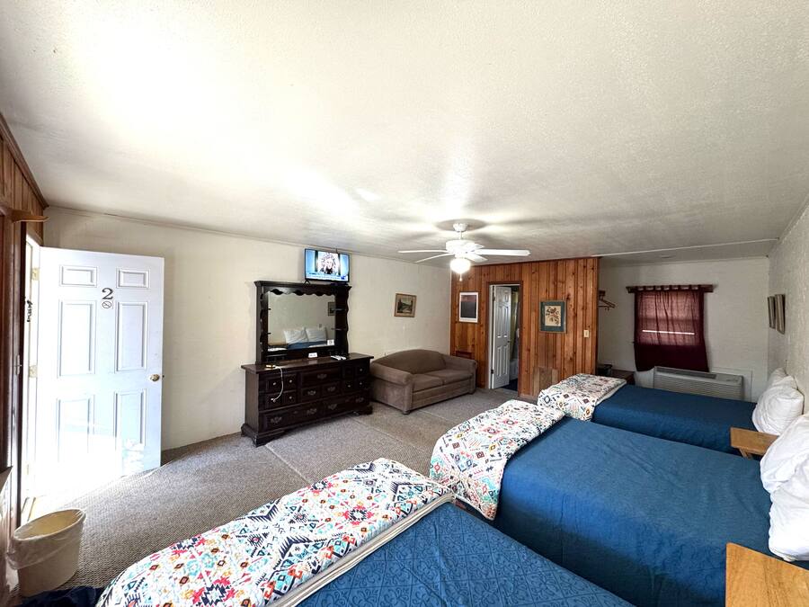 A bedroom with two beds, a dresser, a ceiling fan, and a television on the wall.
