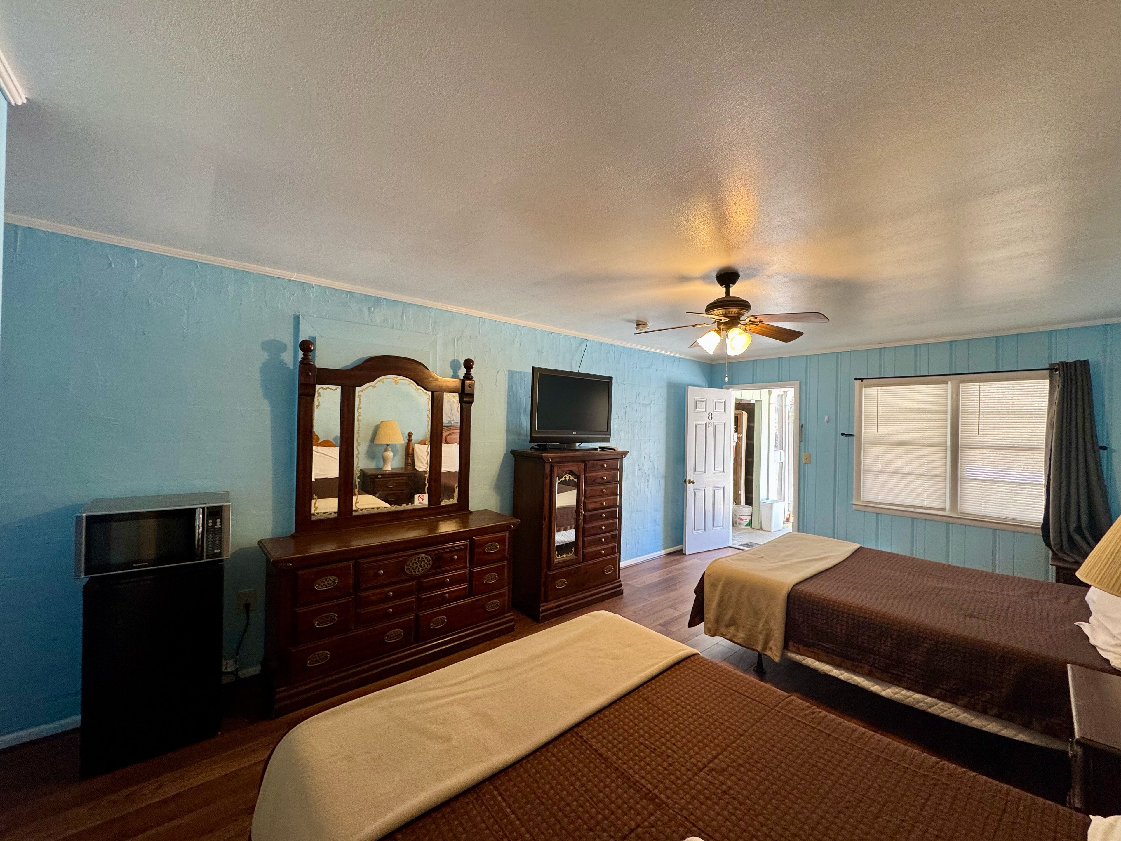 A bedroom with two beds, a dresser, a television, and a ceiling fan.