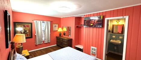 A hotel room with a bed, two bedside lamps, a TV, a mirror, and a bathroom with a sink and toilet.