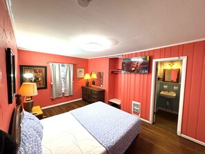 Une chambre d’hôtel comprenant un lit, deux lampes de chevet, une télévision, un miroir et une salle de bain avec un lavabo et des toilettes.