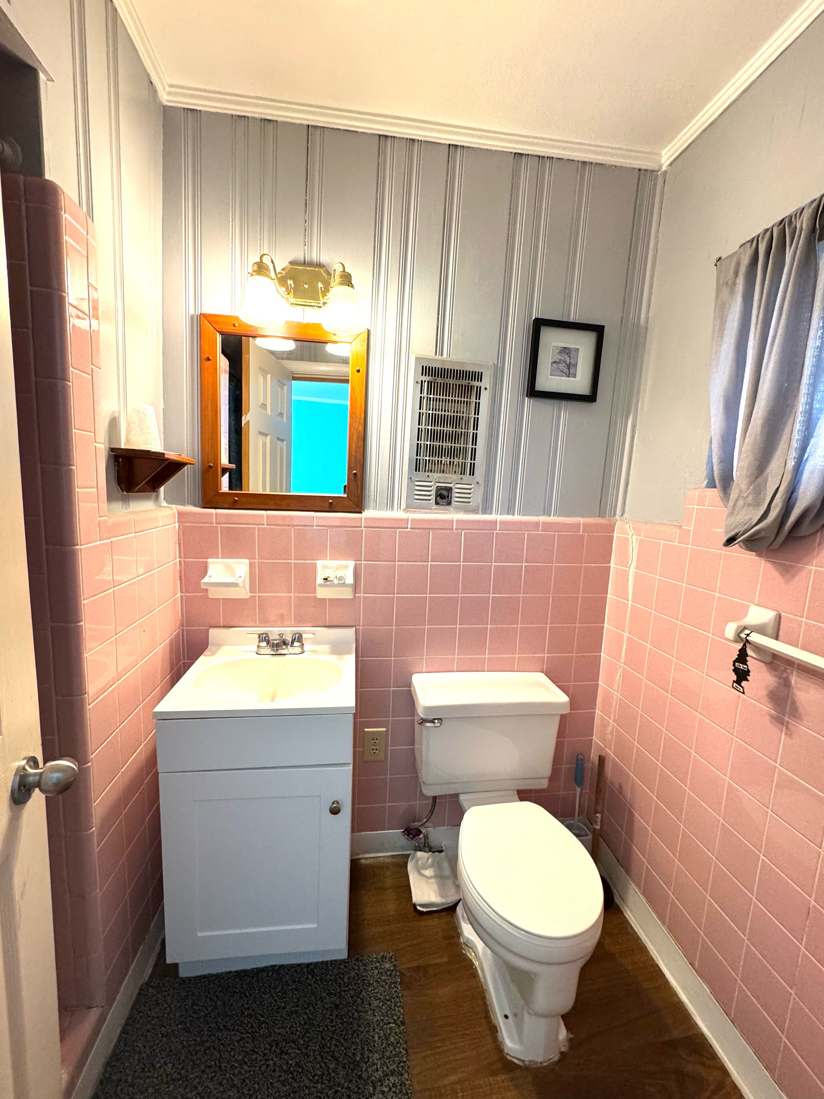 A bathroom with pink tiles, a white sink, a toilet, and a mirror with a light fixture.