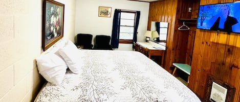 A bedroom with a bed, a desk, a chair, a TV, and a window with curtains.
