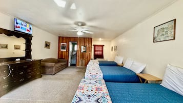 Una camera d'albergo con un letto matrimoniale, due letti singoli, una televisione, un comò e una ventola a soffitto.