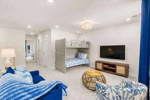 A modern living room with a bunk bed, a television, a round wicker ottoman, and a blue sofa.