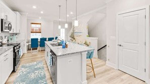 A modern kitchen with white cabinetry, a granite countertop island, and blue bar stools.