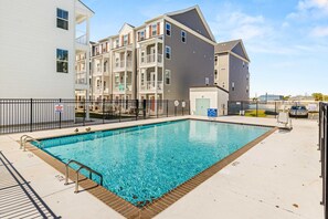 A swimming pool with a metal safety fence, adjacent to multi-story residential buildings.