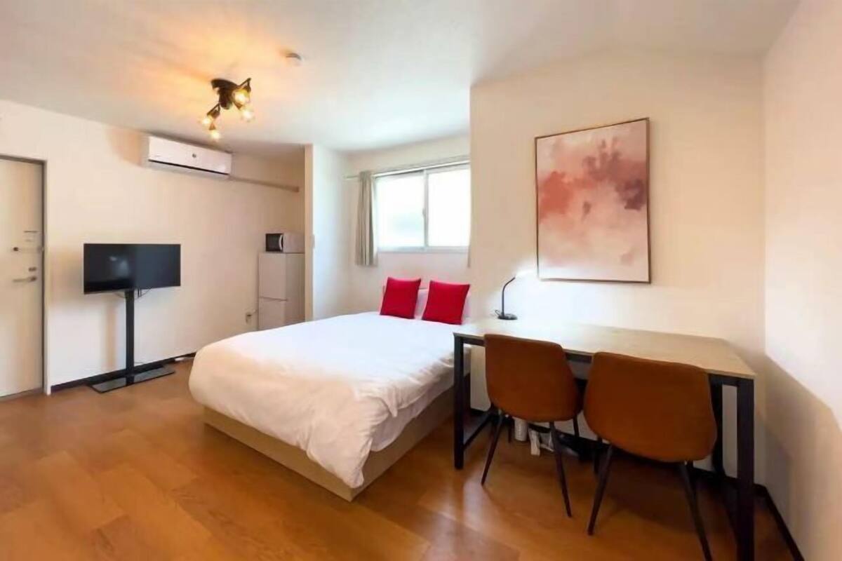 A bedroom with a bed, a desk, two chairs, a television, and a window.