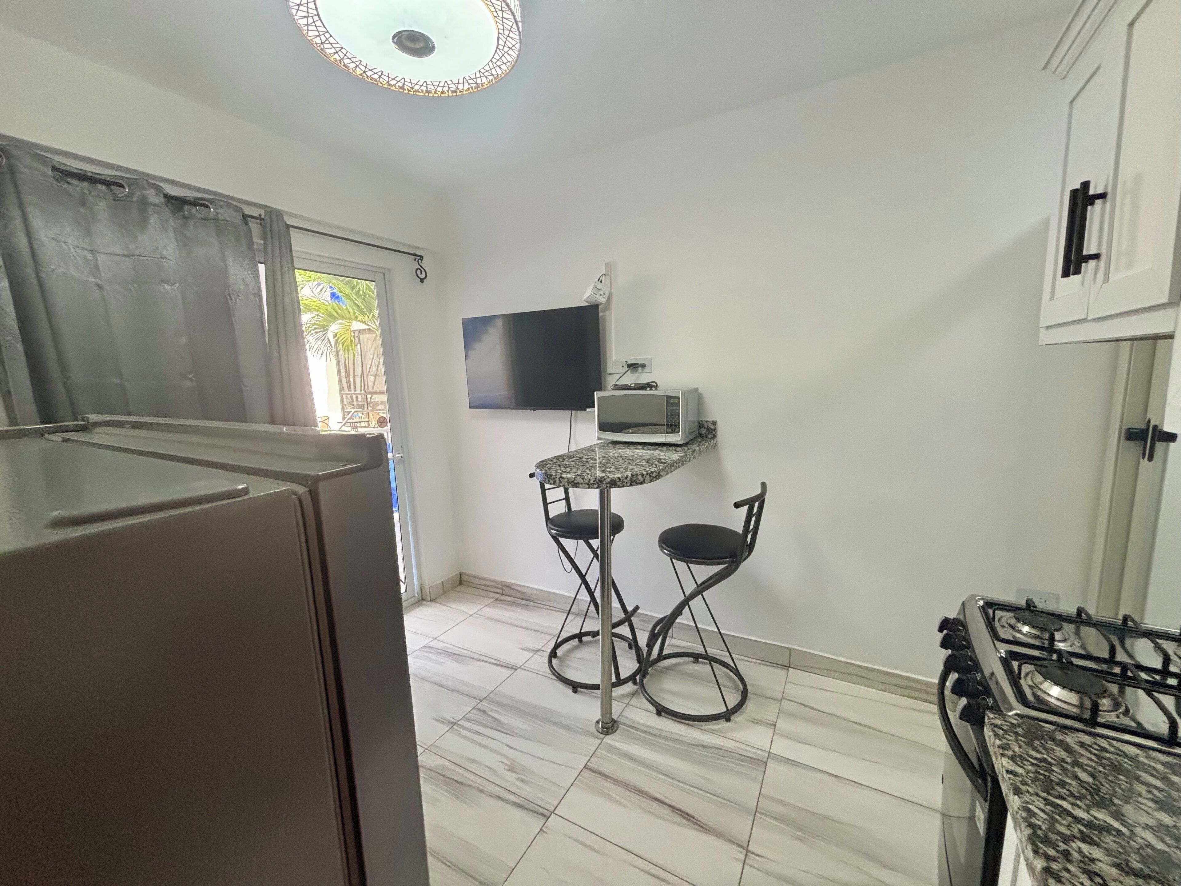 Cocina compacta con refrigerador, microondas, estufa a gas y una pequeña mesa de comedor con dos sillas.