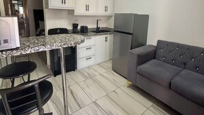 A modern kitchen with white cabinets, a granite countertop, a stainless steel refrigerator, and a grey sofa. - Charming studio in the Heart of Sosua, Facing the pool & at 2 min from the Beach (Sosúa)